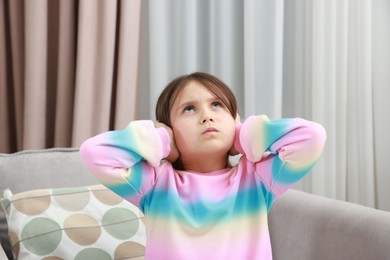 Photo of Annoyed little girl covering her ears with pillows from loud sound on armchair at home