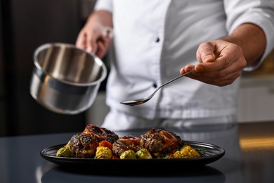 Photo of Professional chef adding sauce to delicious dish at table indoors, closeup