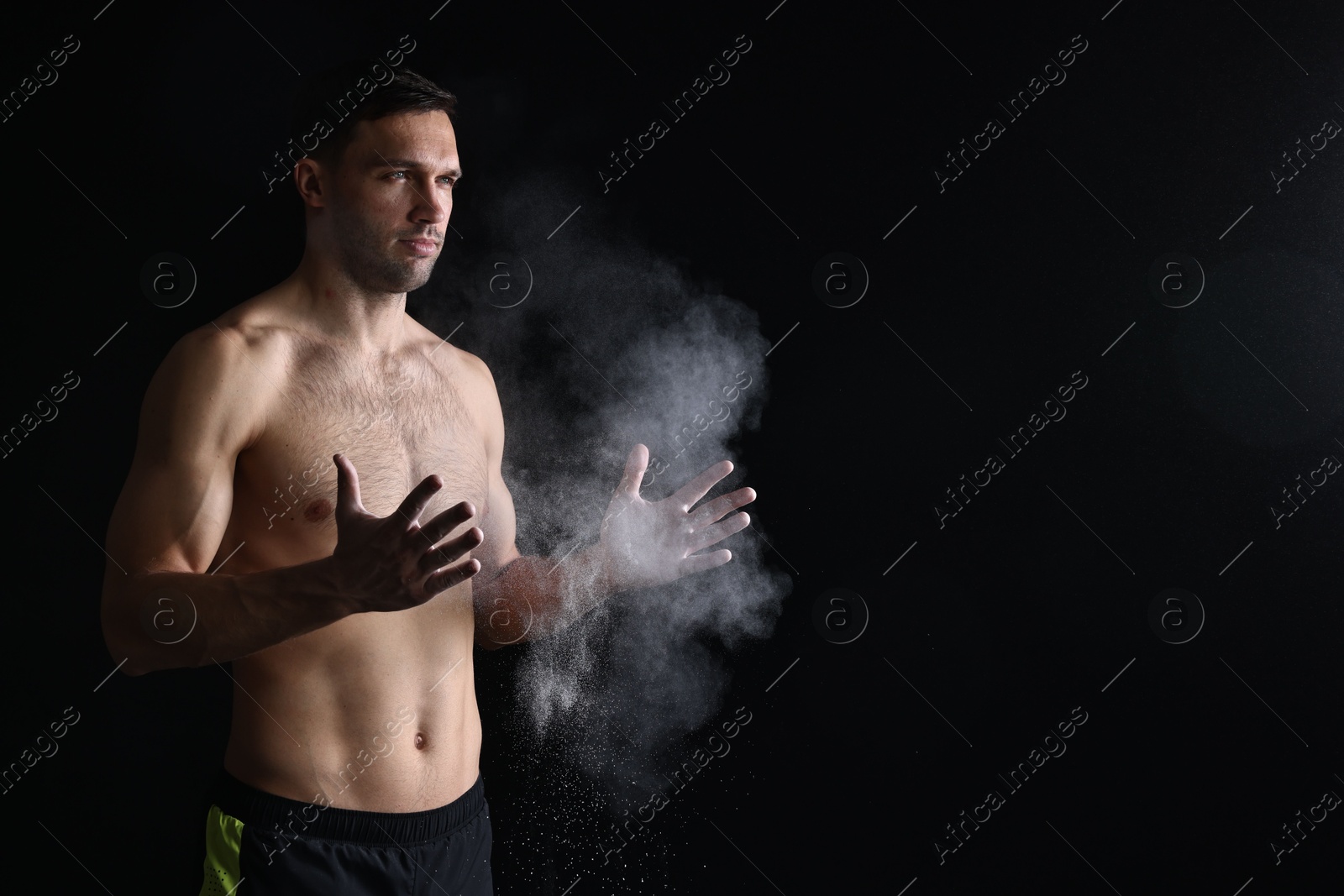 Photo of Man clapping hands with talcum powder before training on black background. Space for text