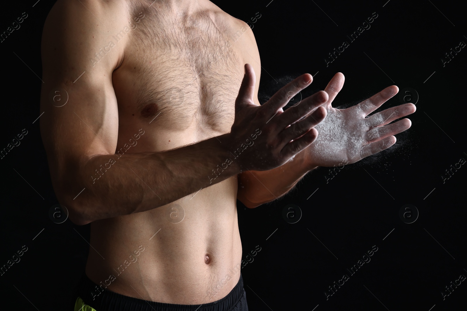 Photo of Man clapping hands with talcum powder before training on black background, closeup