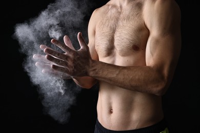 Photo of Man clapping hands with talcum powder before training on black background, closeup