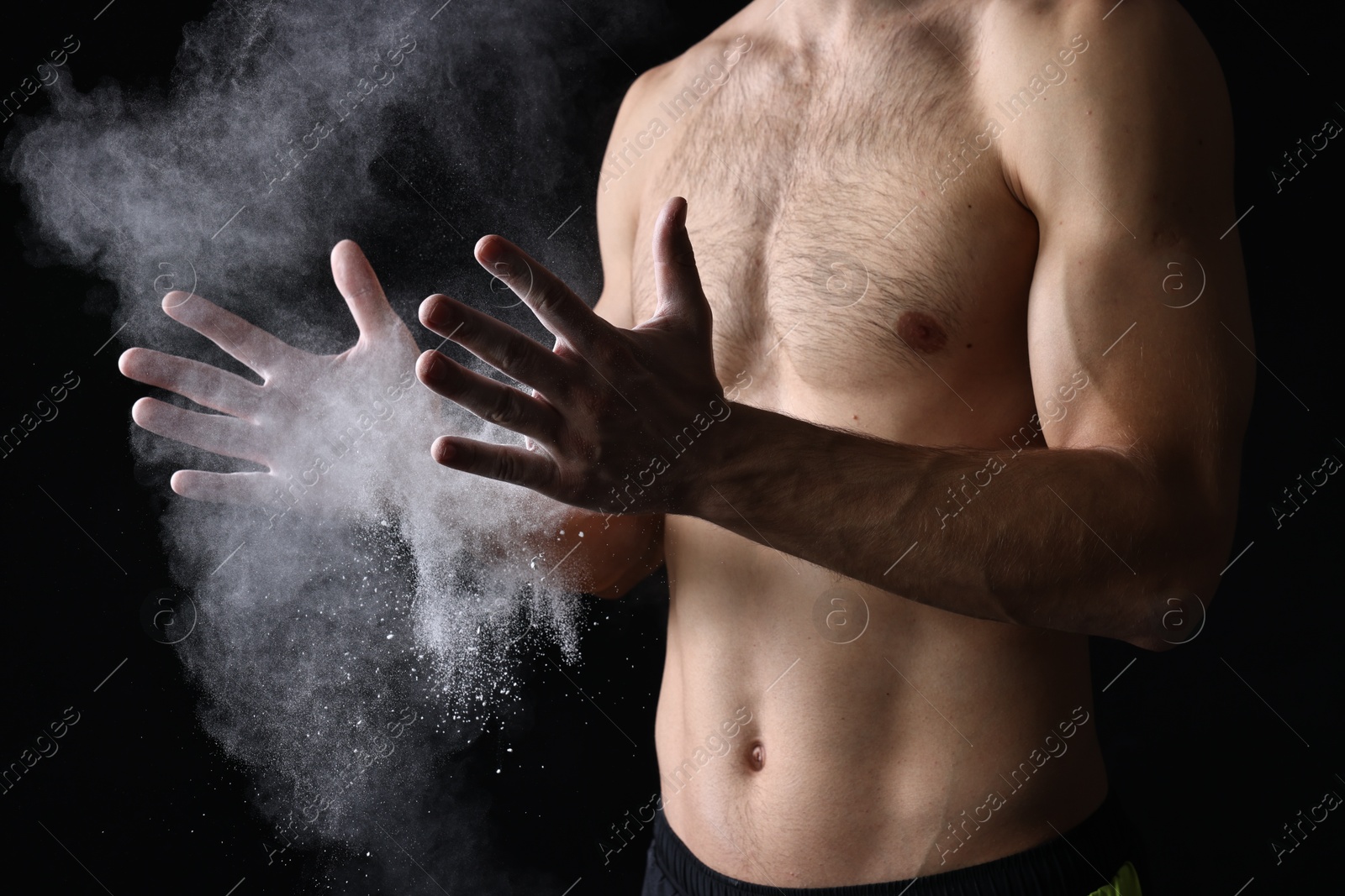 Photo of Man clapping hands with talcum powder before training on black background, closeup