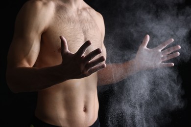 Photo of Man clapping hands with talcum powder before training on black background, closeup