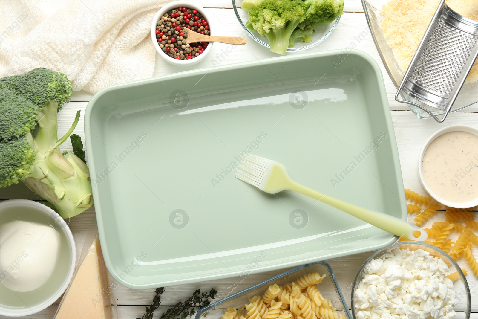 Photo of Ceramic casserole, brush and ingredients on white wooden table, flat lay