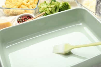 Photo of Ceramic casserole, brush and ingredients on table, closeup