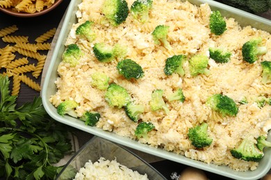 Photo of Uncooked pasta casserole in baking dish and ingredients on wooden table, flat lay