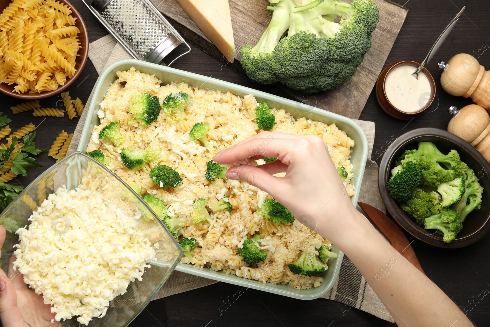 Photo of Woman adding cheese onto pasta casserole at wooden table, top view