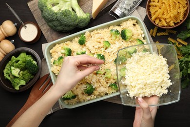 Photo of Woman adding cheese onto pasta casserole at wooden table, top view