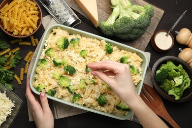 Photo of Woman adding cheese onto pasta casserole at wooden table, top view