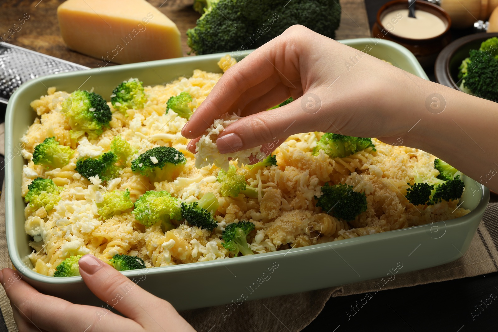 Photo of Woman adding cheese onto pasta casserole at table, closeup