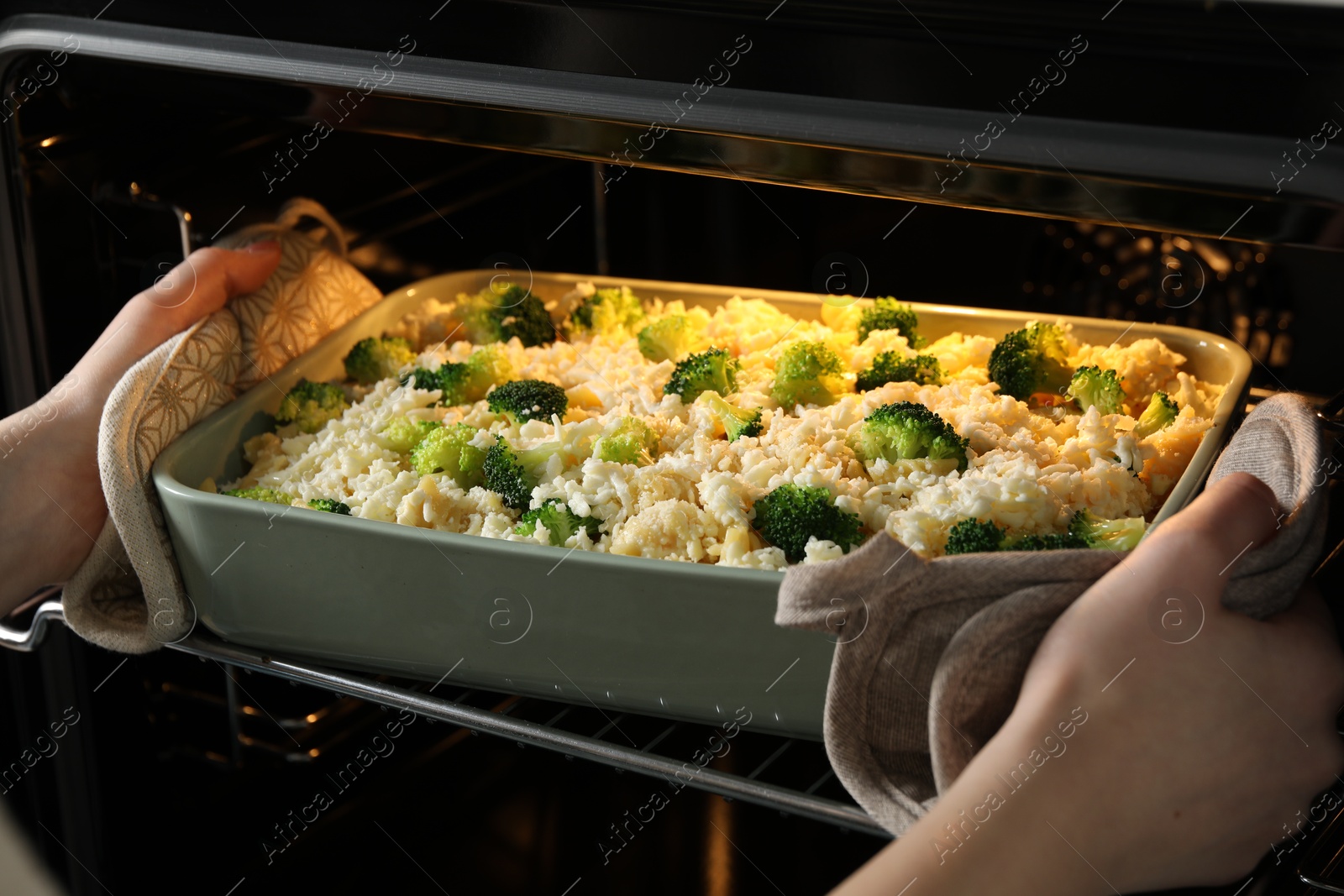 Photo of Woman putting dish with uncooked pasta casserole into oven indoors, closeup