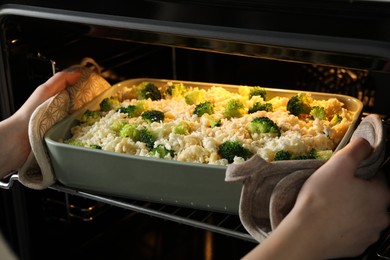 Photo of Woman putting dish with uncooked pasta casserole into oven indoors, closeup