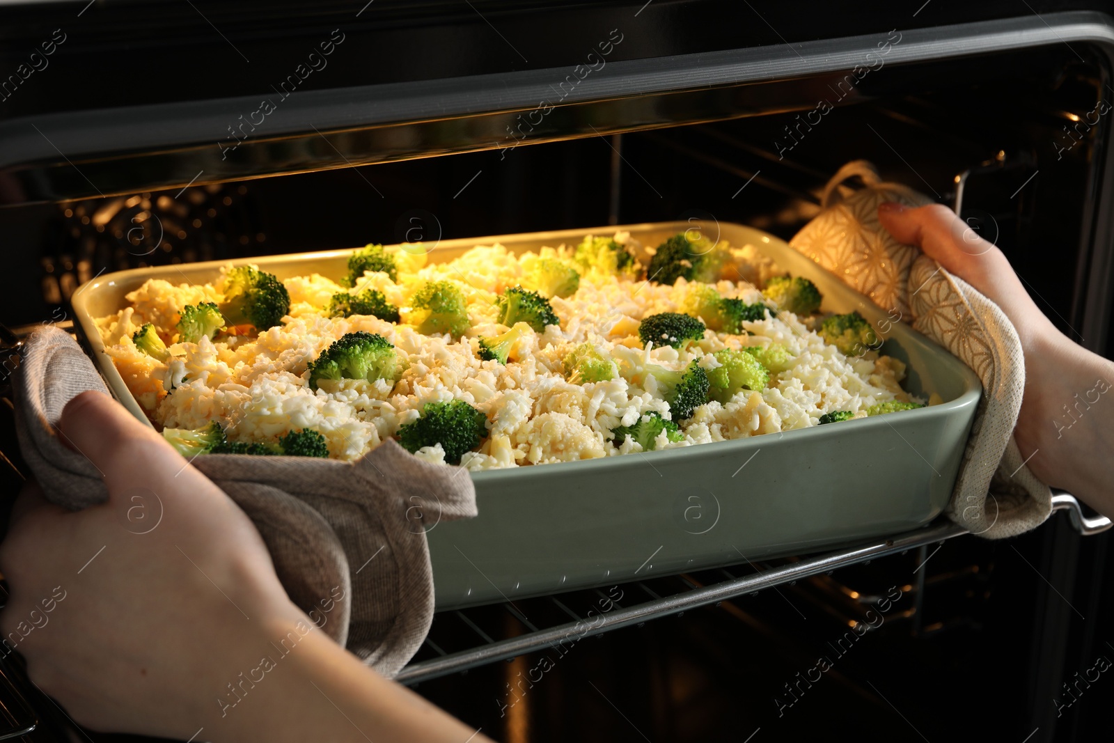 Photo of Woman putting dish with uncooked pasta casserole into oven indoors, closeup