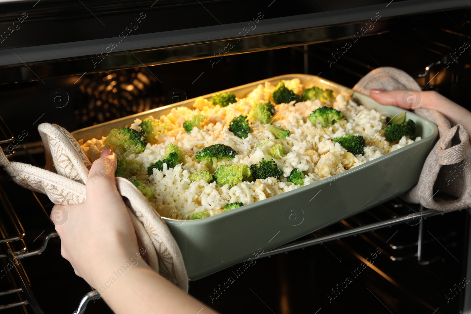 Photo of Woman putting dish with uncooked pasta casserole into oven indoors, closeup