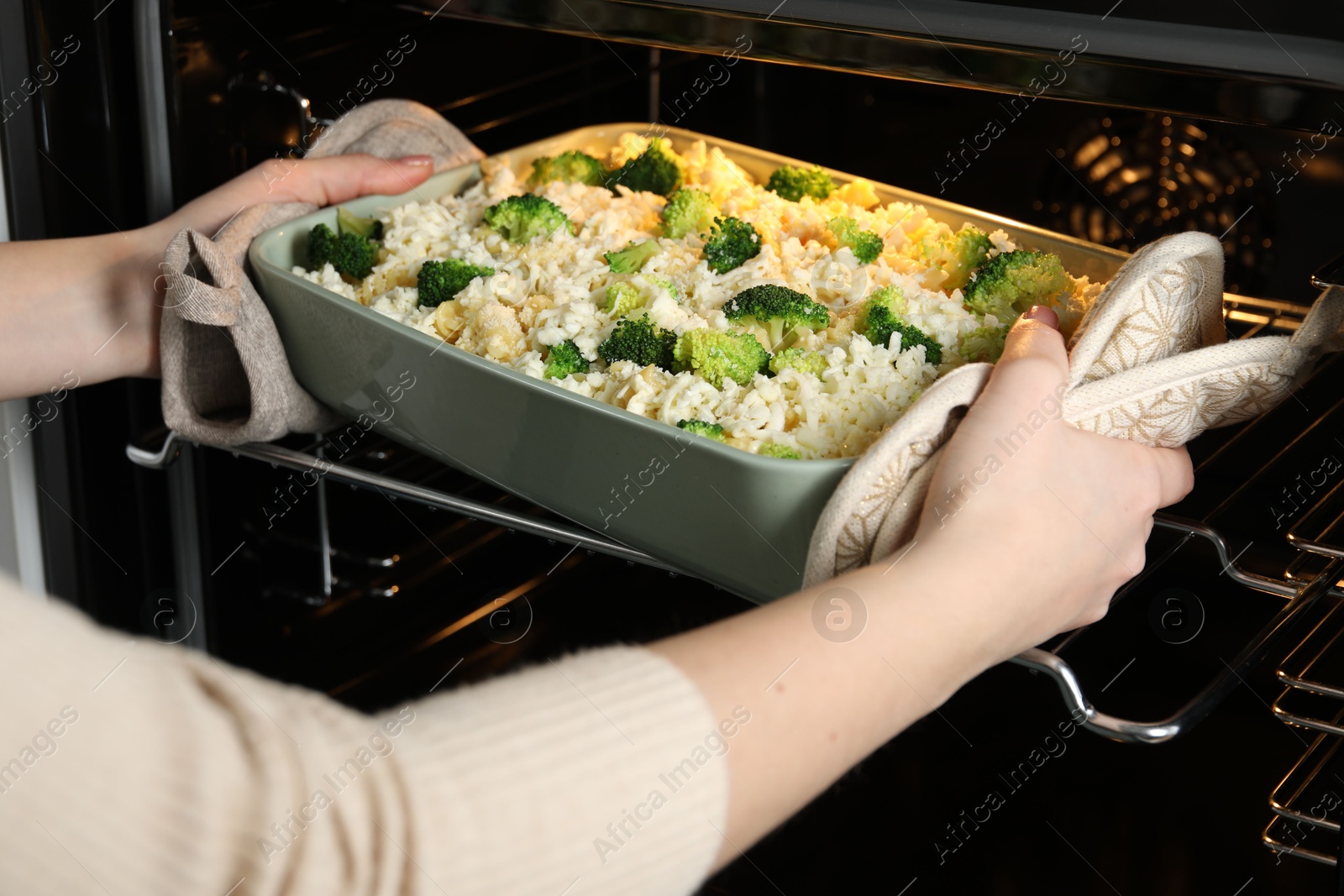 Photo of Woman putting dish with uncooked pasta casserole into oven indoors, closeup