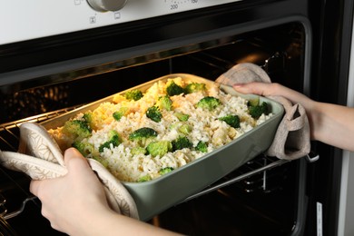 Photo of Woman putting dish with uncooked pasta casserole into oven indoors, closeup