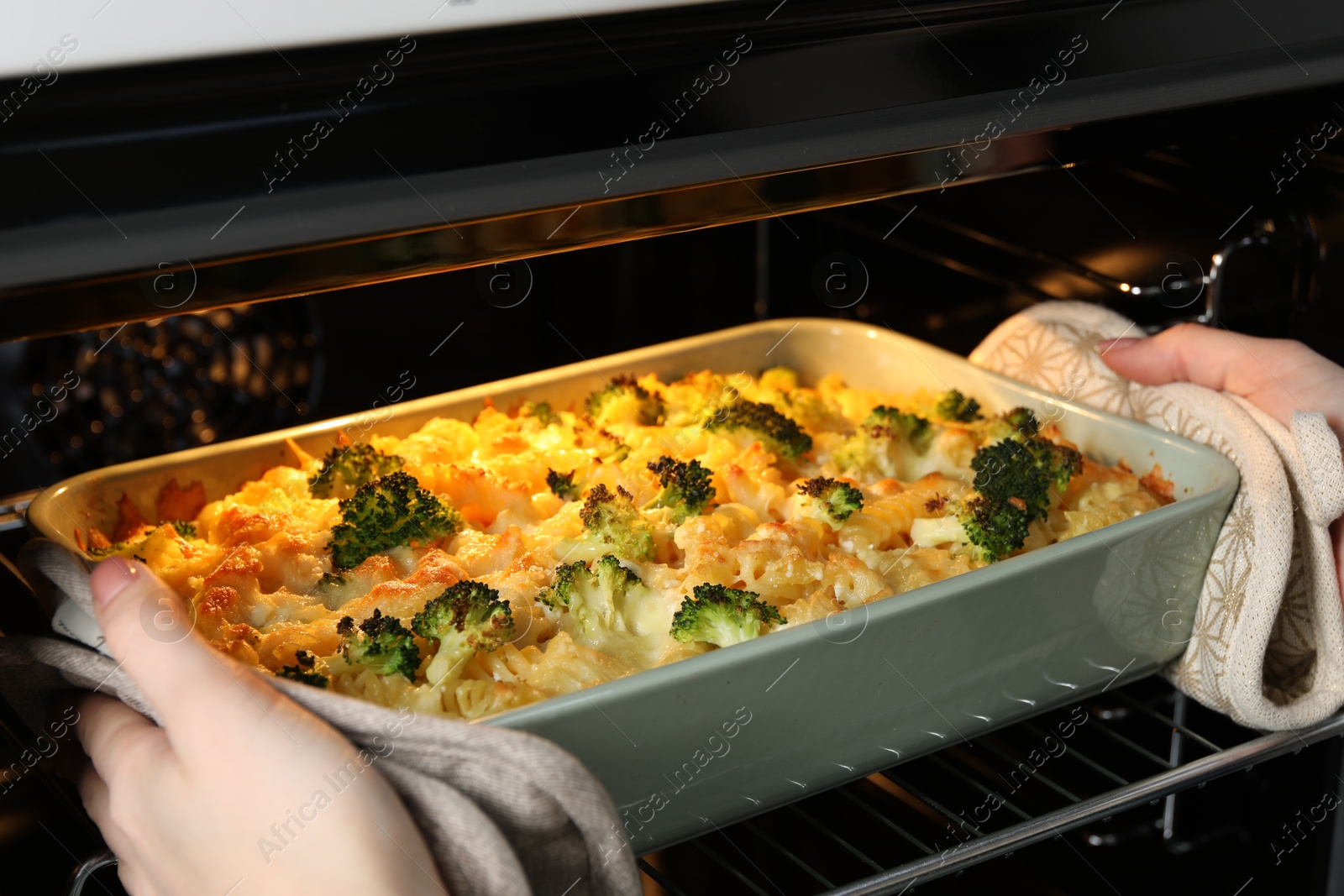 Photo of Woman taking tasty pasta casserole out of oven indoors, closeup