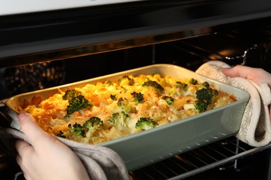 Photo of Woman taking tasty pasta casserole out of oven indoors, closeup