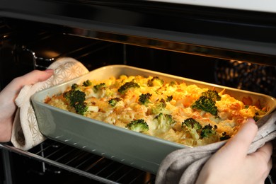 Photo of Woman taking tasty pasta casserole out of oven indoors, closeup