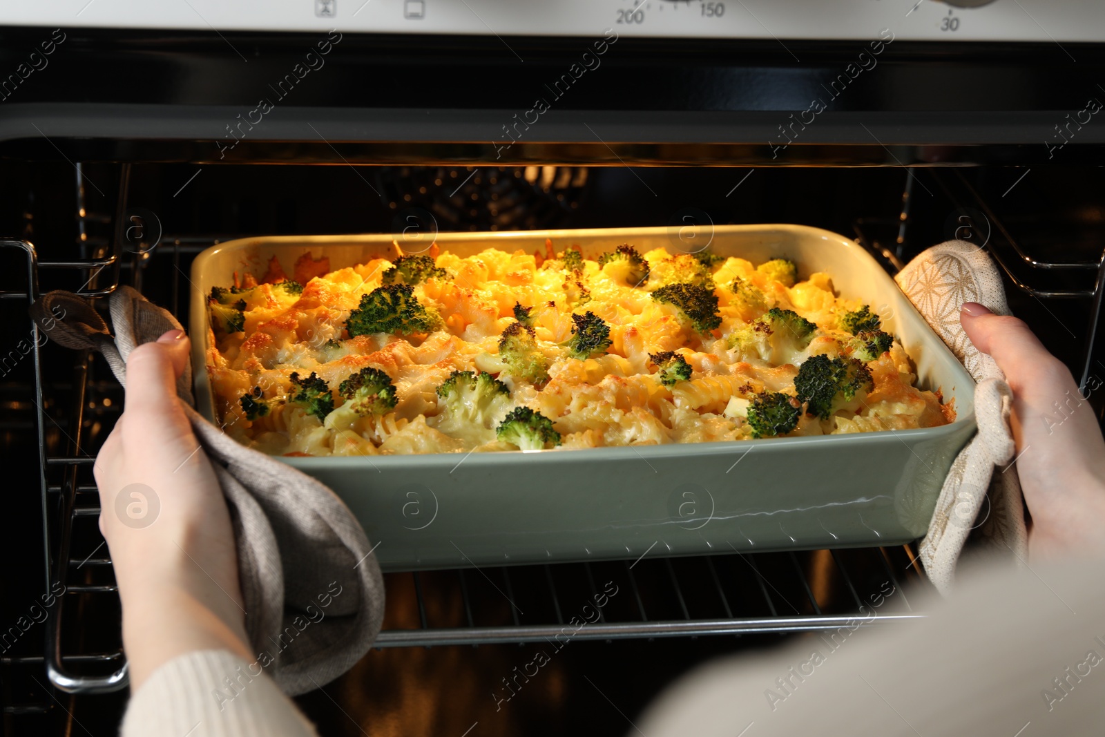 Photo of Woman taking tasty pasta casserole out of oven indoors, closeup