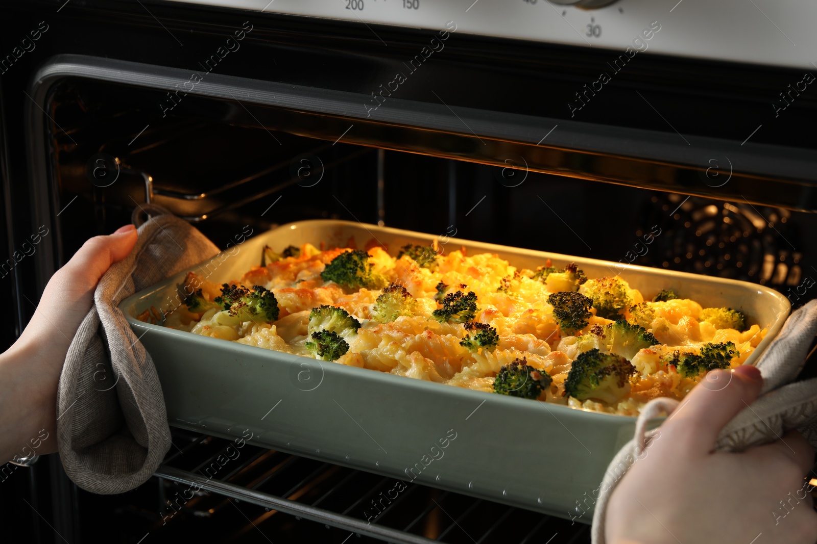 Photo of Woman taking tasty pasta casserole out of oven indoors, closeup