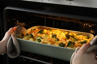 Photo of Woman taking tasty pasta casserole out of oven indoors, closeup