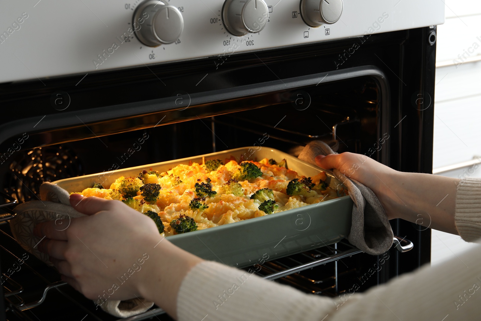 Photo of Woman taking tasty pasta casserole out of oven indoors, closeup