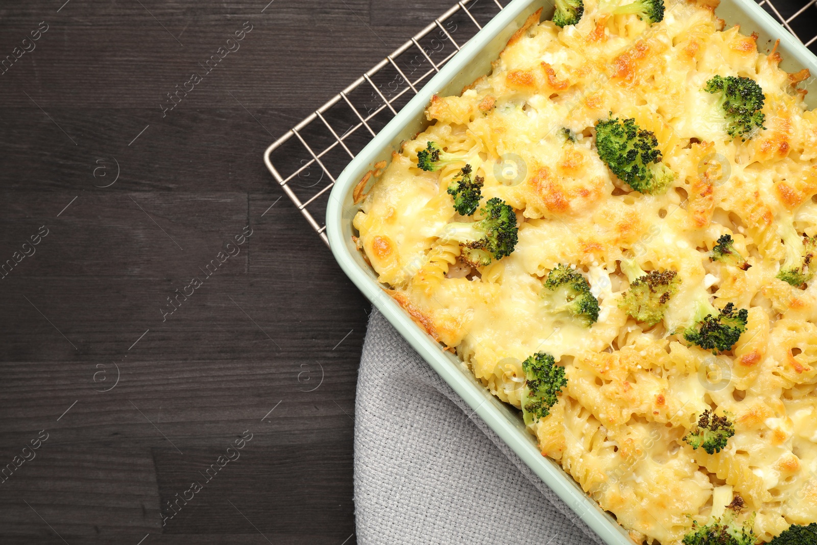 Photo of Tasty pasta casserole with cheese and broccoli in baking dish on wooden table, top view. Space for text