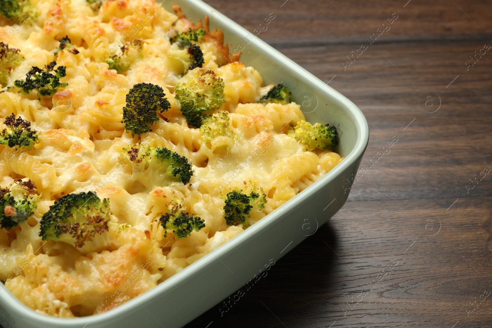 Photo of Tasty pasta casserole with cheese and broccoli in baking dish on wooden table, closeup