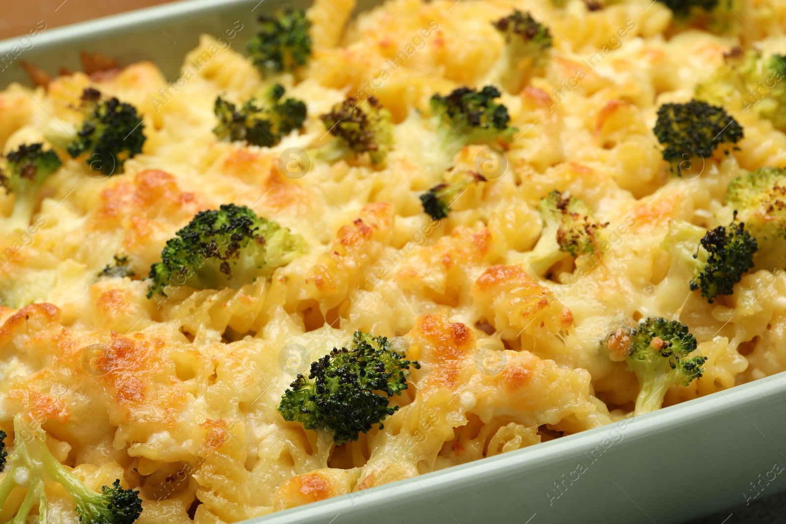 Photo of Tasty pasta casserole with cheese and broccoli in baking dish on table, closeup