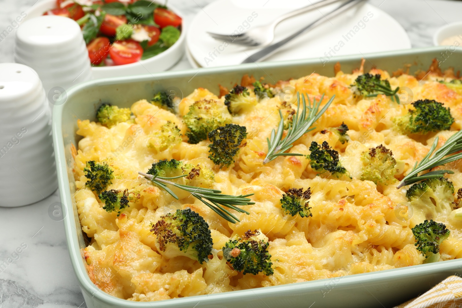 Photo of Tasty pasta casserole with cheese, rosemary and broccoli in baking dish on white marble table, closeup