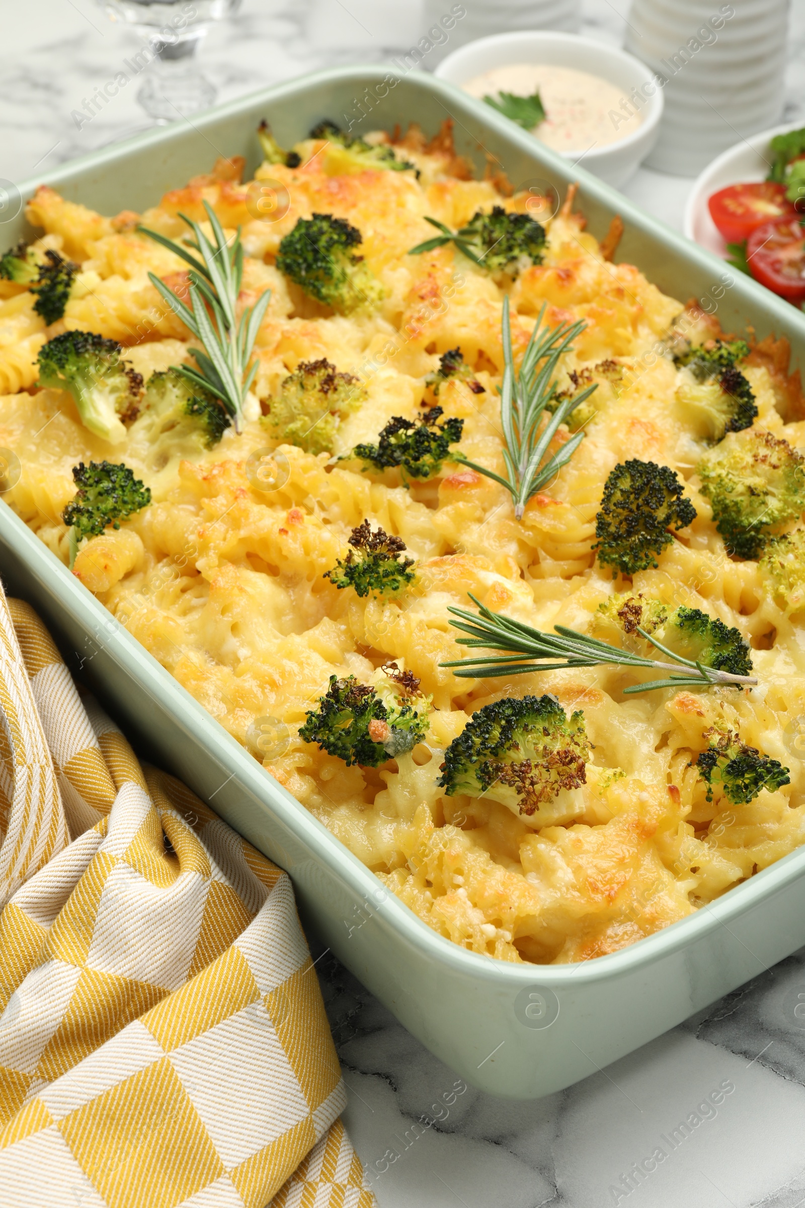 Photo of Tasty pasta casserole with cheese, rosemary and broccoli in baking dish on white marble table, closeup