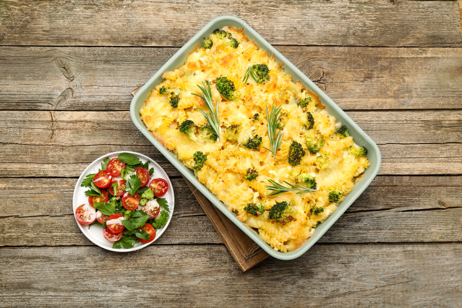 Photo of Tasty pasta casserole with cheese, rosemary, broccoli and salad on wooden table, top view