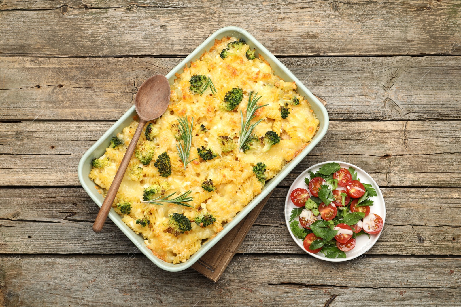 Photo of Tasty pasta casserole with cheese, rosemary, broccoli and salad on wooden table, top view