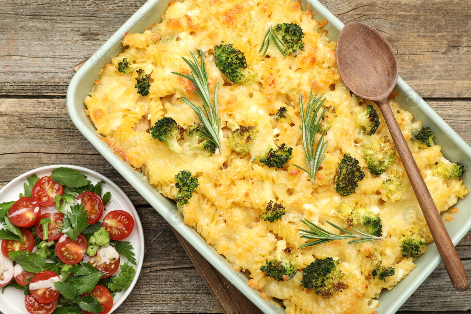 Photo of Tasty pasta casserole with cheese, rosemary, broccoli and salad on wooden table, top view