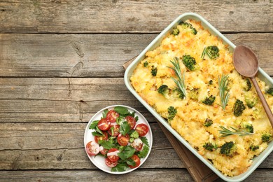 Photo of Tasty pasta casserole with cheese, rosemary, broccoli and salad on wooden table, top view. Space for text