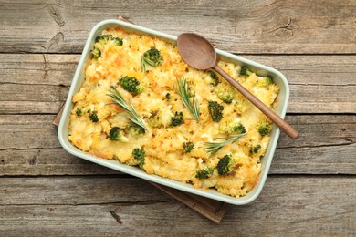 Photo of Tasty pasta casserole with cheese, rosemary and broccoli in baking dish on wooden table, top view