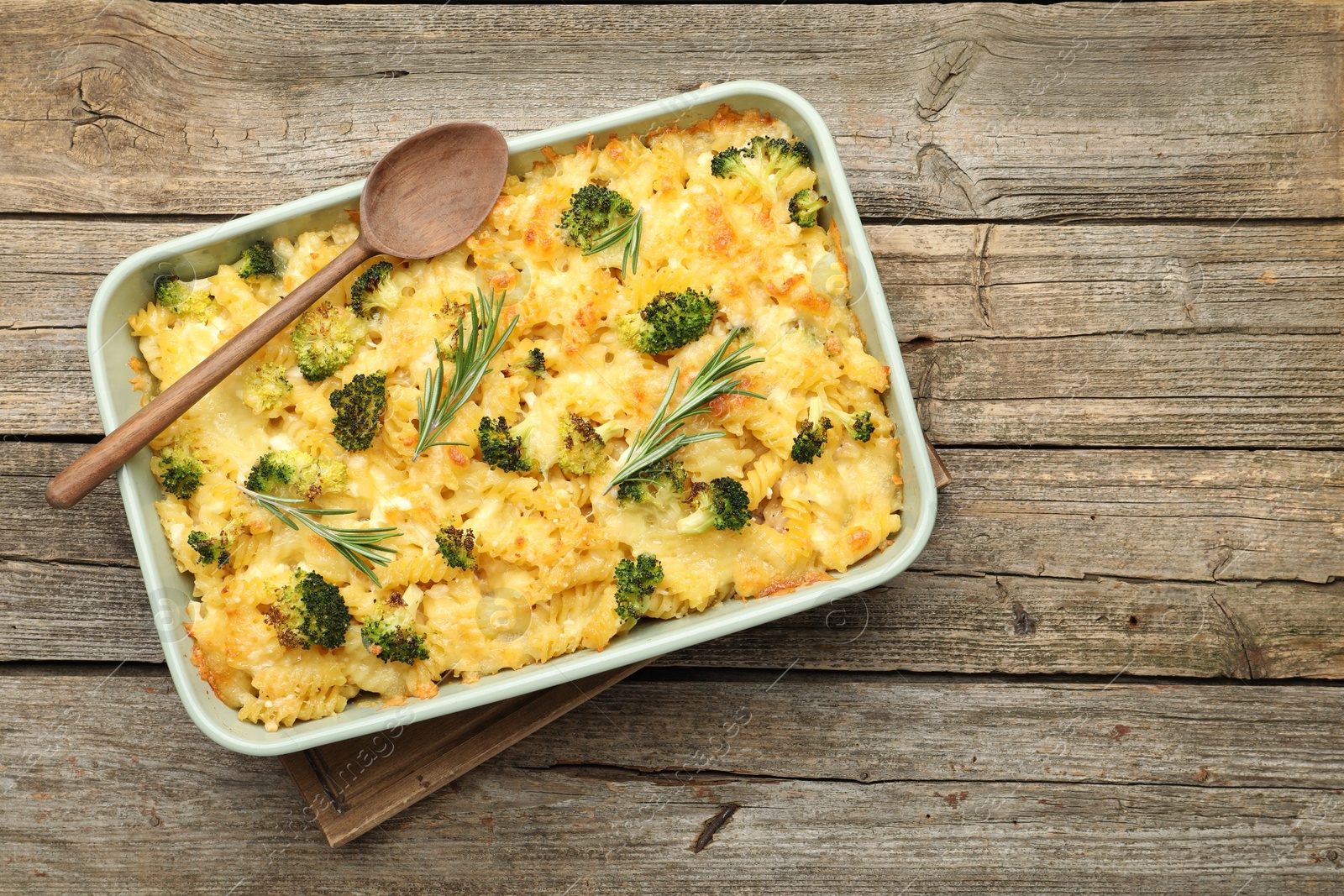 Photo of Tasty pasta casserole with cheese, rosemary and broccoli in baking dish on wooden table, top view. Space for text