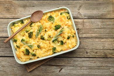 Photo of Tasty pasta casserole with cheese, rosemary and broccoli in baking dish on wooden table, top view. Space for text