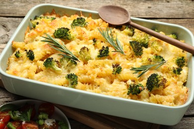 Photo of Tasty pasta casserole with cheese, rosemary, broccoli and salad on wooden table, closeup