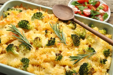 Photo of Tasty pasta casserole with cheese, rosemary, broccoli and salad on table, closeup