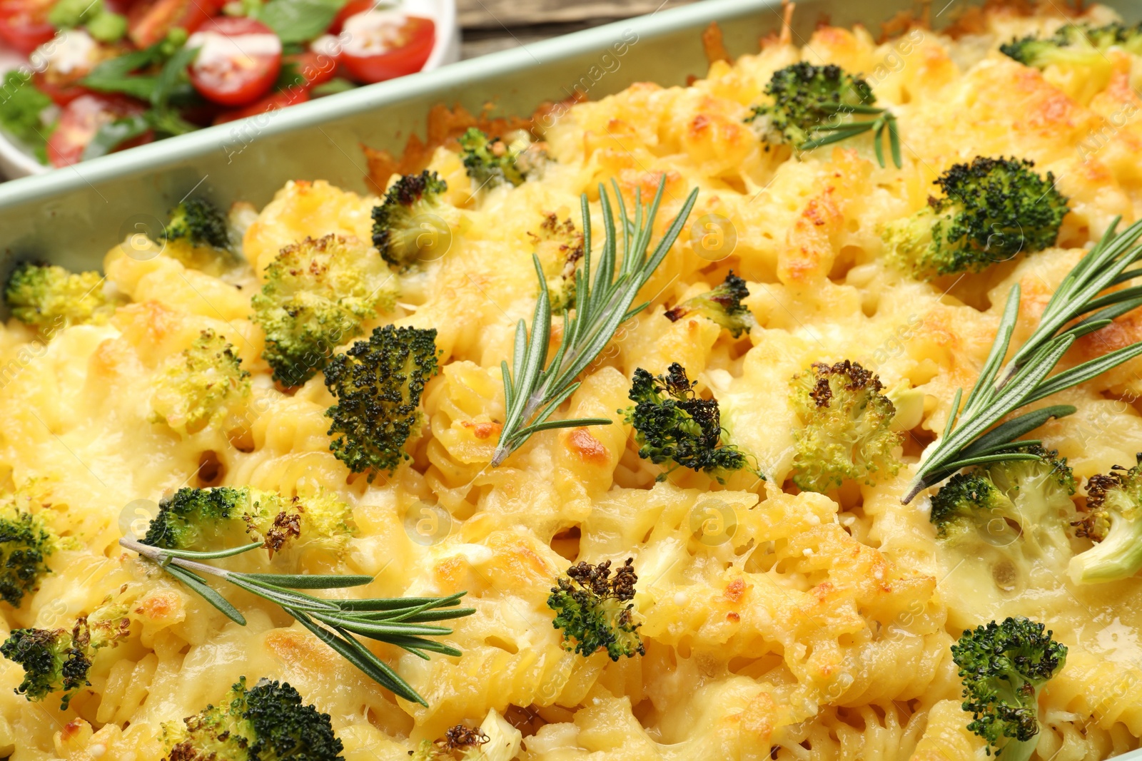 Photo of Tasty pasta casserole with cheese, rosemary, broccoli and salad on table, closeup