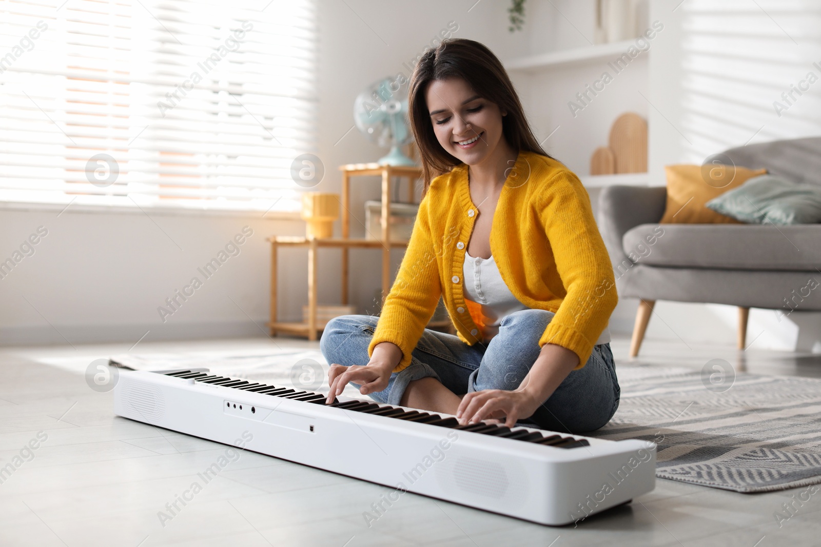 Photo of Smiling woman playing synthesizer on floor at home