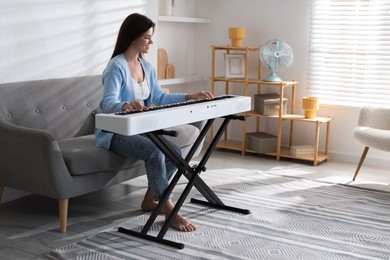 Photo of Smiling woman playing synthesizer at home. Electronic musical instrument