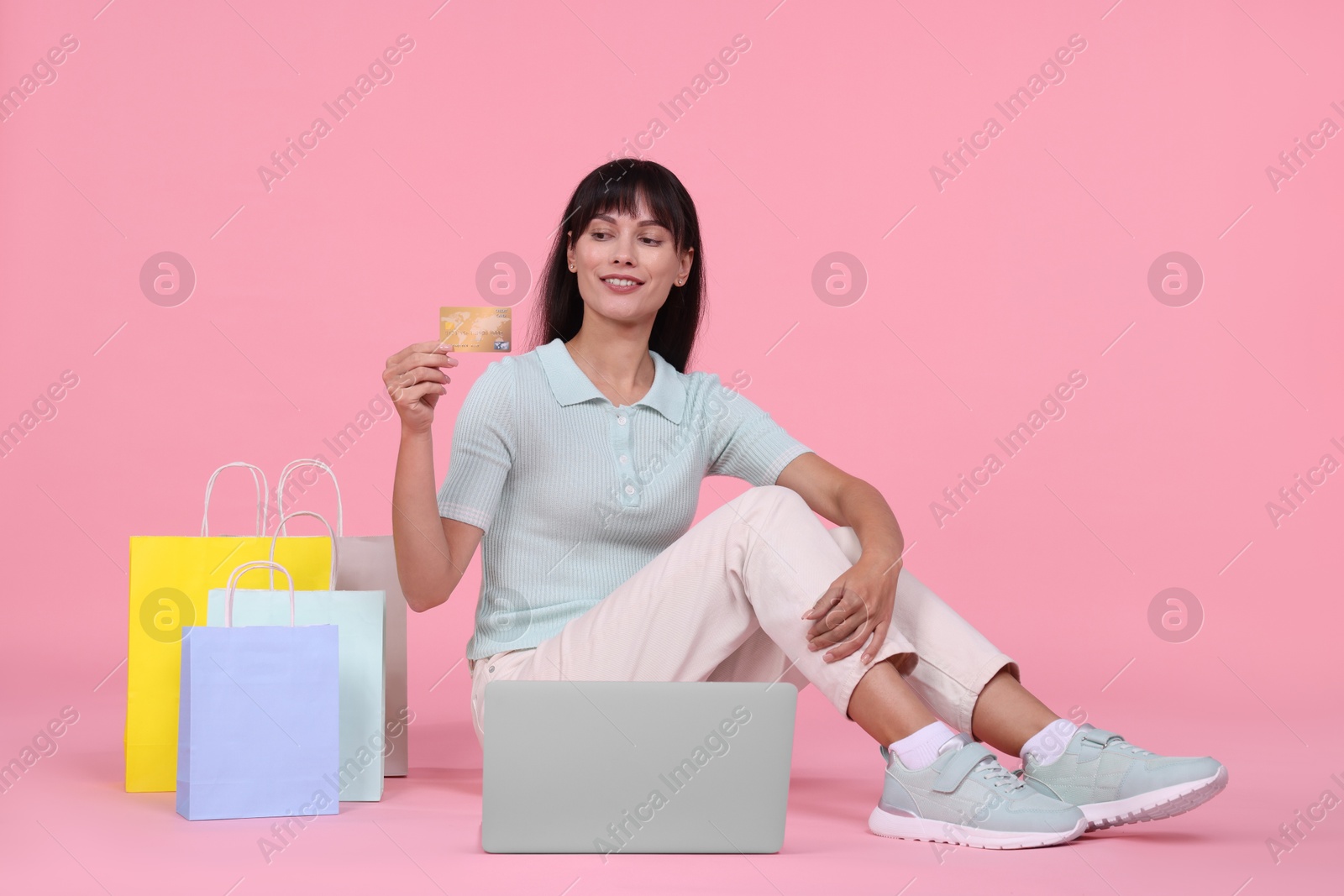 Photo of Internet shopping. Happy woman with credit card, laptop and colorful bags on pink background