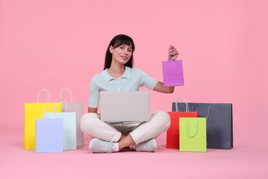 Photo of Internet shopping. Happy woman with laptop and colorful bags on pink background