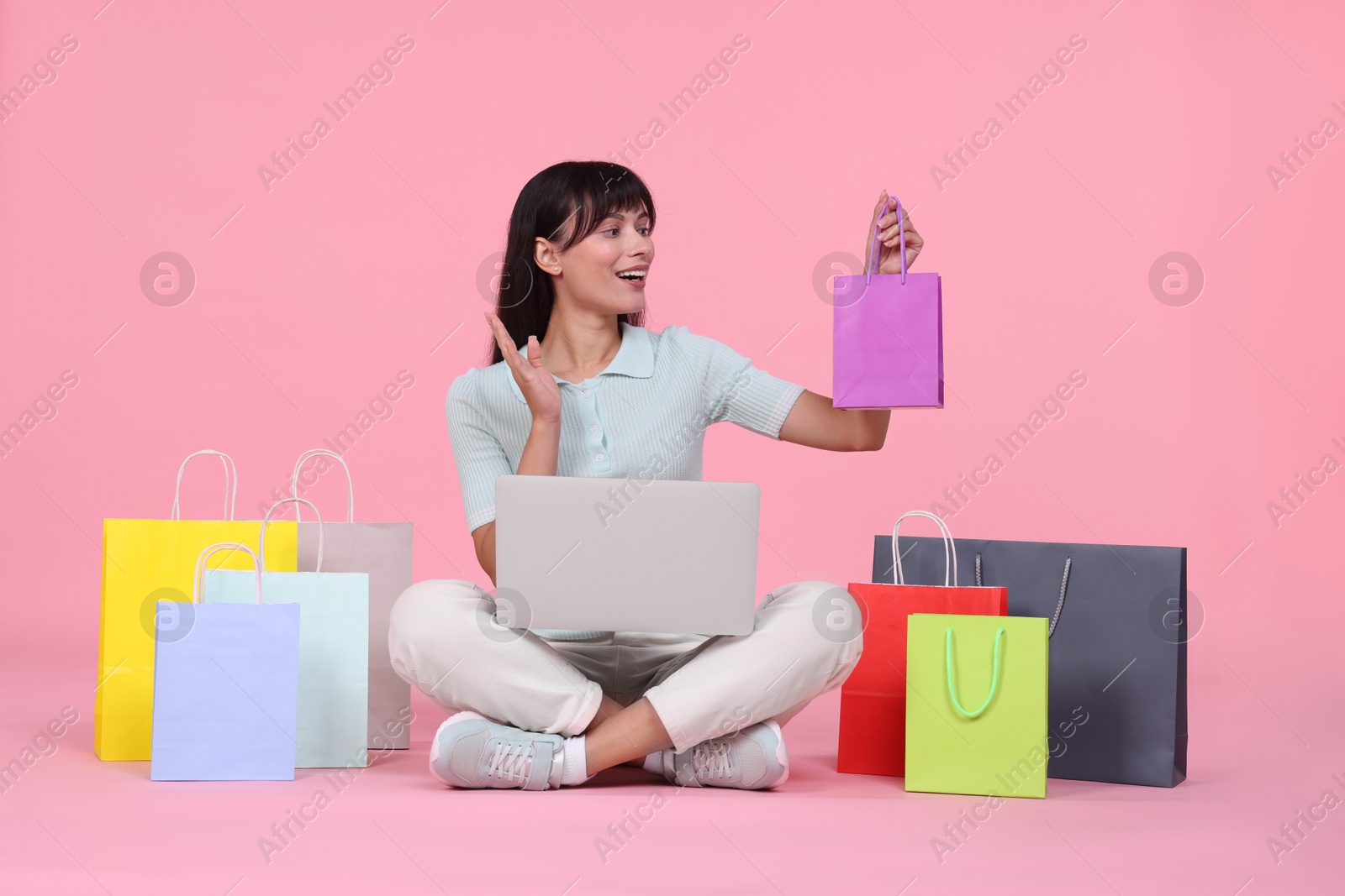 Photo of Internet shopping. Happy woman with laptop and colorful bags on pink background