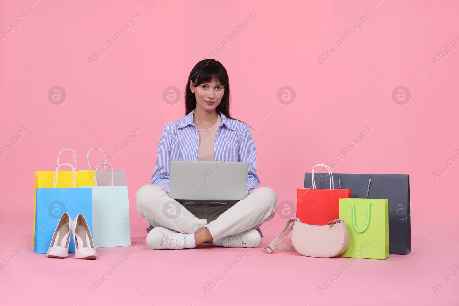 Photo of Internet shopping. Beautiful woman with laptop and colorful bags on pink background