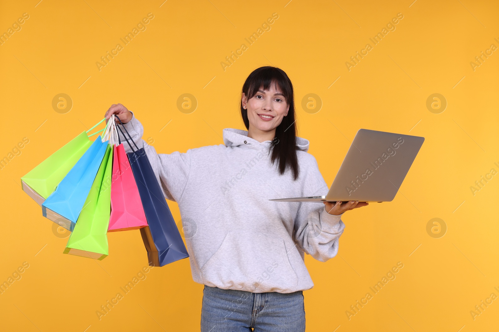 Photo of Internet shopping. Happy woman with laptop and colorful bags on orange background