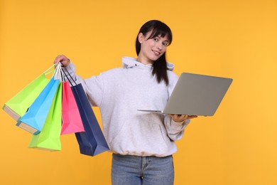 Photo of Internet shopping. Happy woman with laptop and colorful bags on orange background